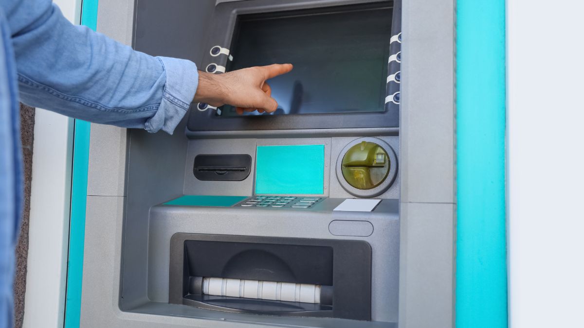Egy személy mutat az ATM érintőképernyőjére, készpénzfelvétel előtt.