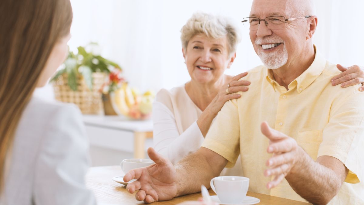 Idősebb pár beszélget egy fiatal nővel, kávé mellett, baráti légkörben.