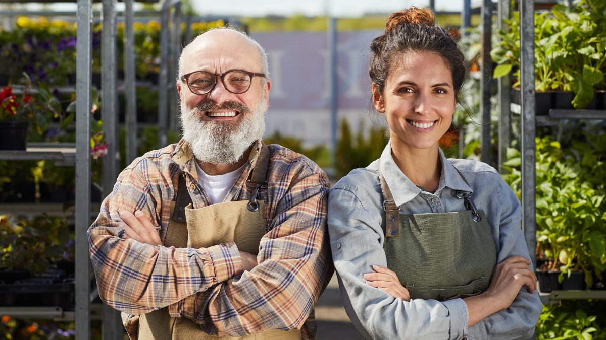 Egy idős férfi és egy fiatal nő mosolyogva állnak egy növényekkel teli üvegházban.