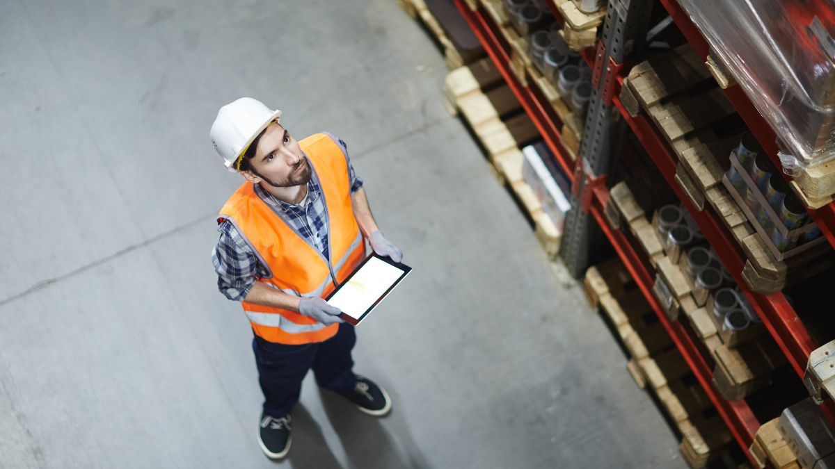 Raktáros tabletet használ a leltározás során, figyelmesen nézve a polcokat.