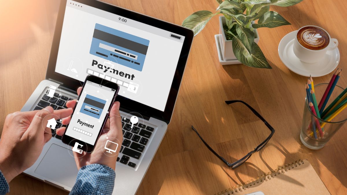 Egy felhasználó mobiltelefonon online vásárlást végez, laptop előtt ülve.