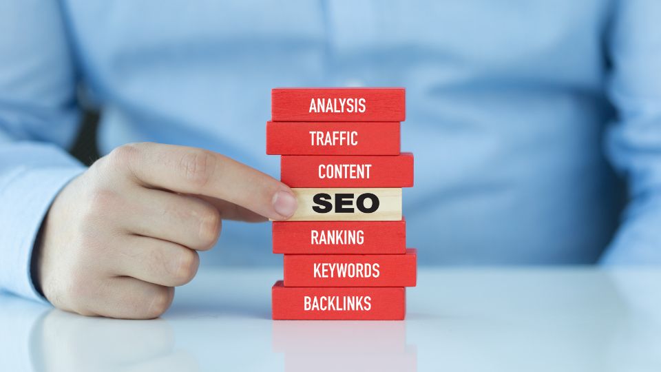 Egy kéz mutat a SEO feliratra, amely piros blokkok között helyezkedik el.