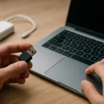 USB dongle in hand next to a laptop on a wooden surface.